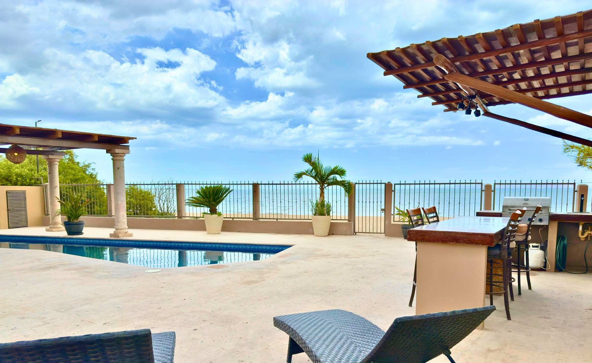An outdoor pool area with a pergola, seating, and a grill.