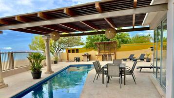 Ein Poolbereich mit einer Pergola, Liegestühlen und Meerblick.