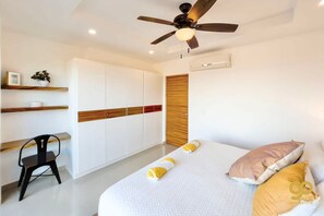 A modern bedroom with a bed, a ceiling fan, built-in wardrobes, and a small desk with a chair. - Oceanfront Escape: Pool, BBQ, & Sunset Views (El Centenario)
