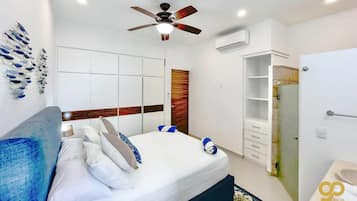 A modern hotel room with a bed, a ceiling fan, a wardrobe, and a bathroom with a sink and mirror.