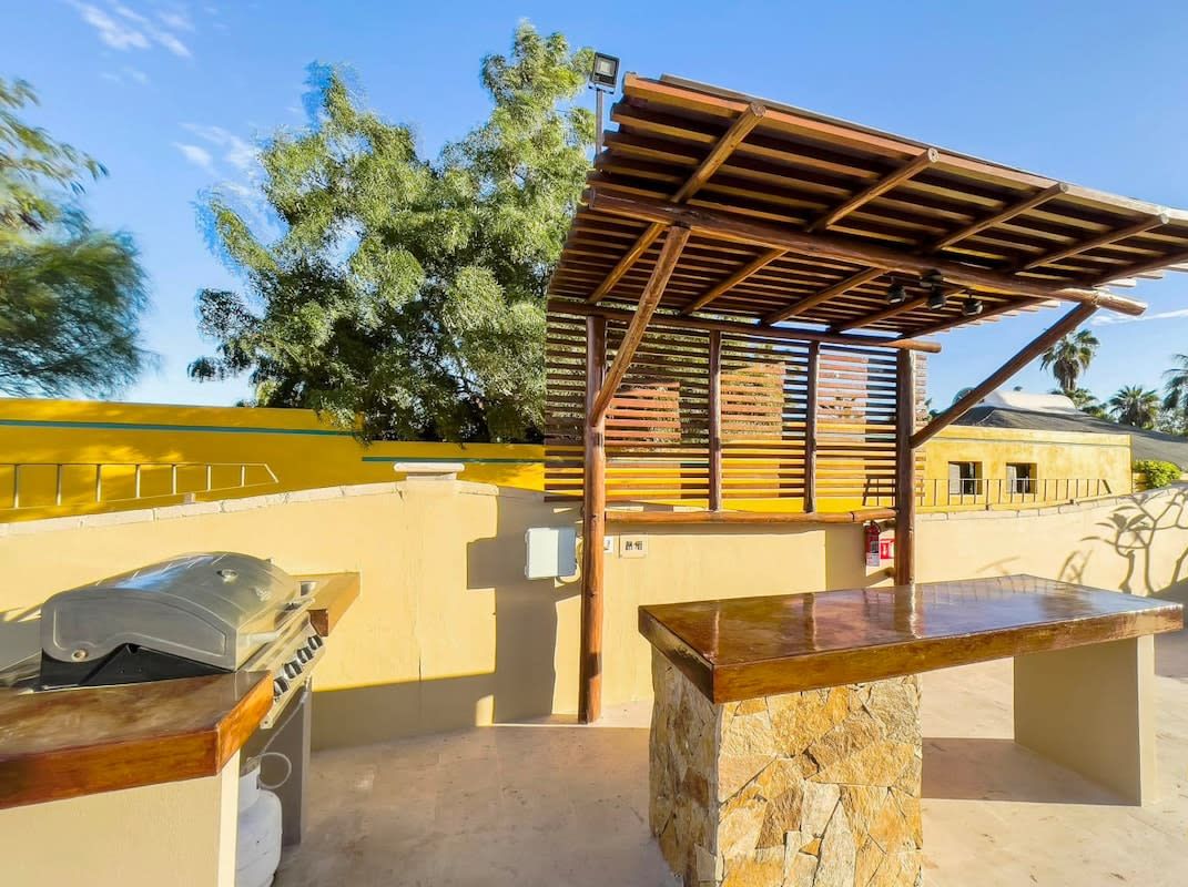 An outdoor patio area with a stone bench, a grill, and a wooden pergola structure.