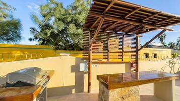 An outdoor patio area with a stone bench, a grill, and a wooden pergola structure.
