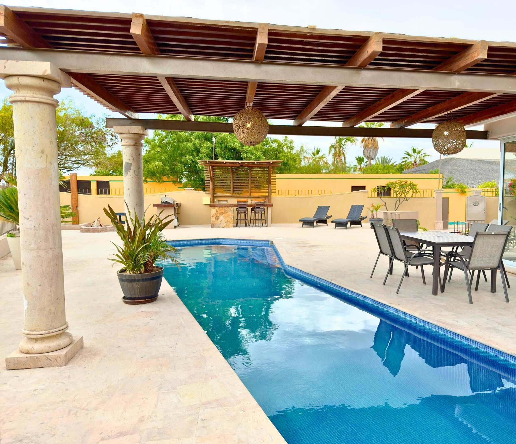 Ein Swimmingpool mit einer Pergola, Liegestühlen und einer Bar.