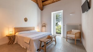 A bedroom with a bed, bedside table, lamp, wooden bench, and a chair.