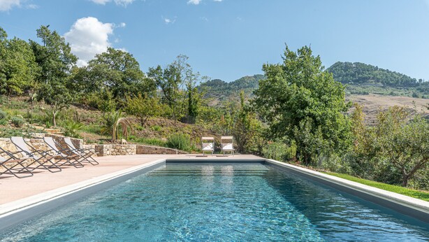 A rectangular swimming pool with clear blue water, surrounded by a stone deck and white lounge chairs.