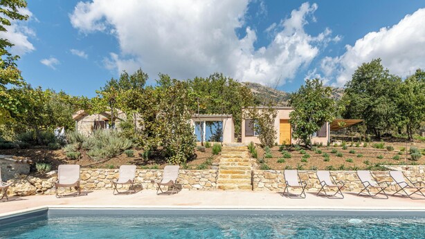 A poolside view of a property with a stone pathway leading to a building, surrounded by trees and a clear sky. - Borgo Le Niche by Wonderful Italy - Calliope (Polizzi Generosa)