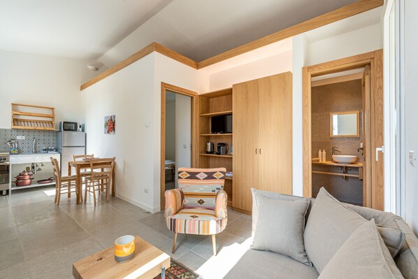 A modern living room with a sofa, a wooden coffee table, a patterned armchair, and a dining area with a table and chairs.