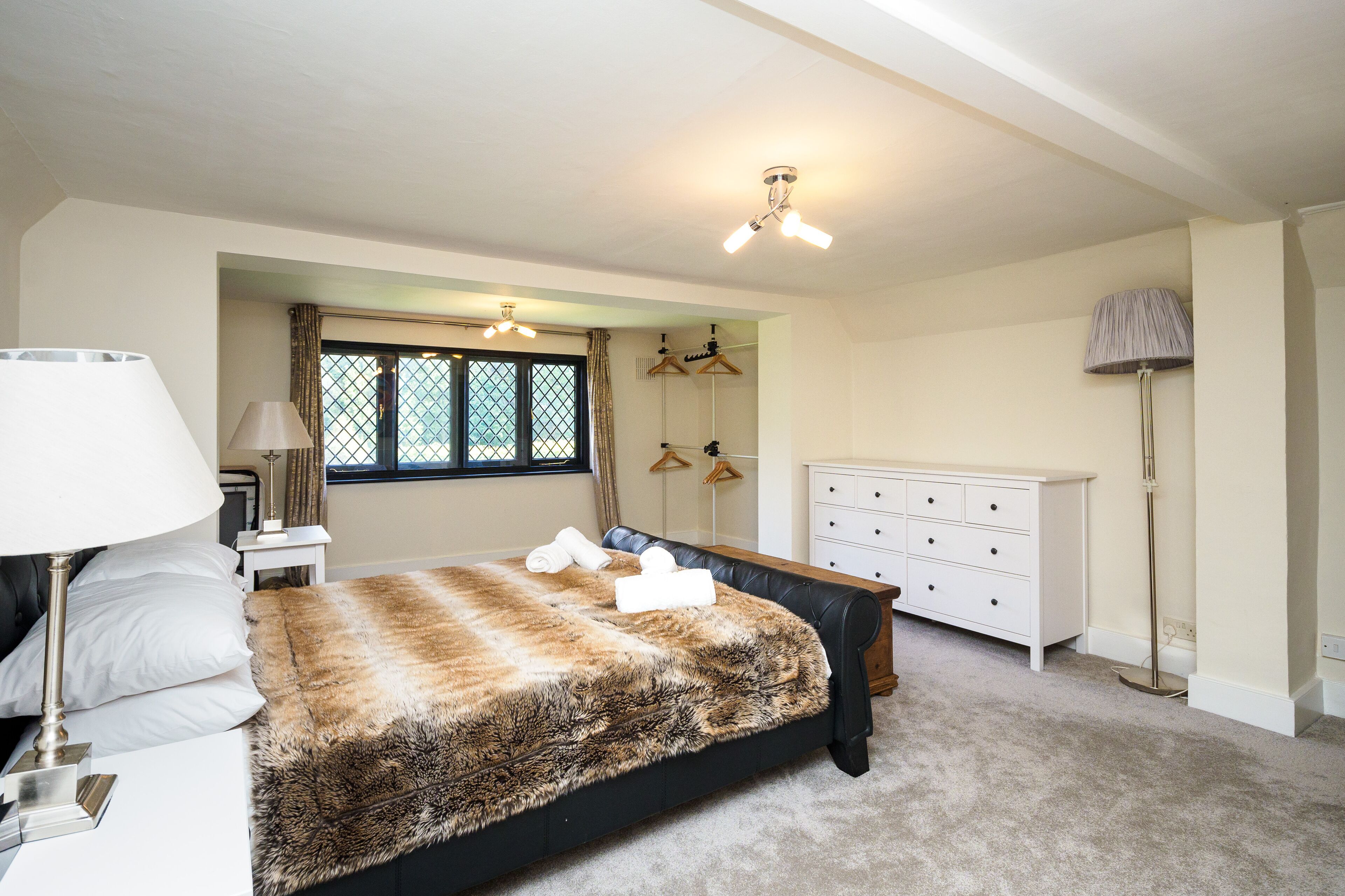 A bedroom with a bed, a dresser, a lamp, a window with curtains, and a ceiling fan.