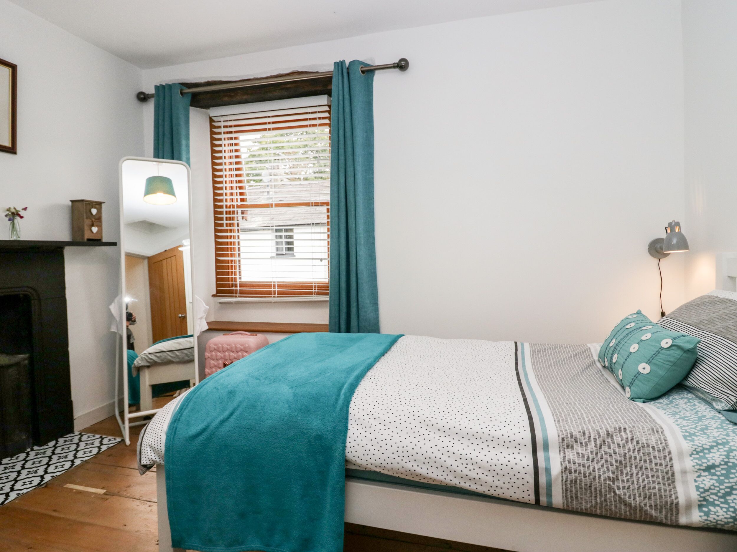 A bedroom with a bed, a bedside lamp, a window with curtains, a dresser, and a mirror.