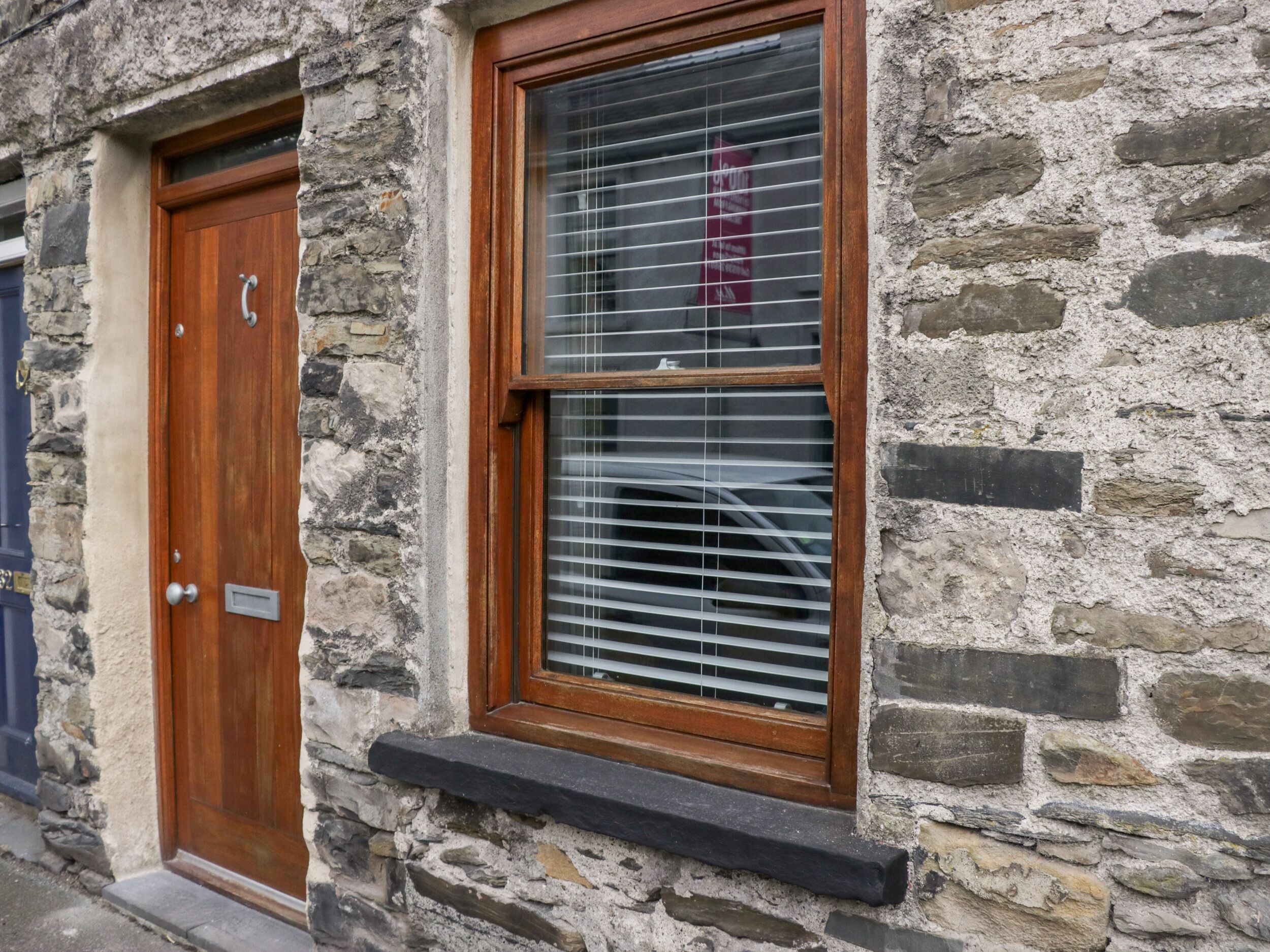 A stone building with a wooden door and a window with blinds.