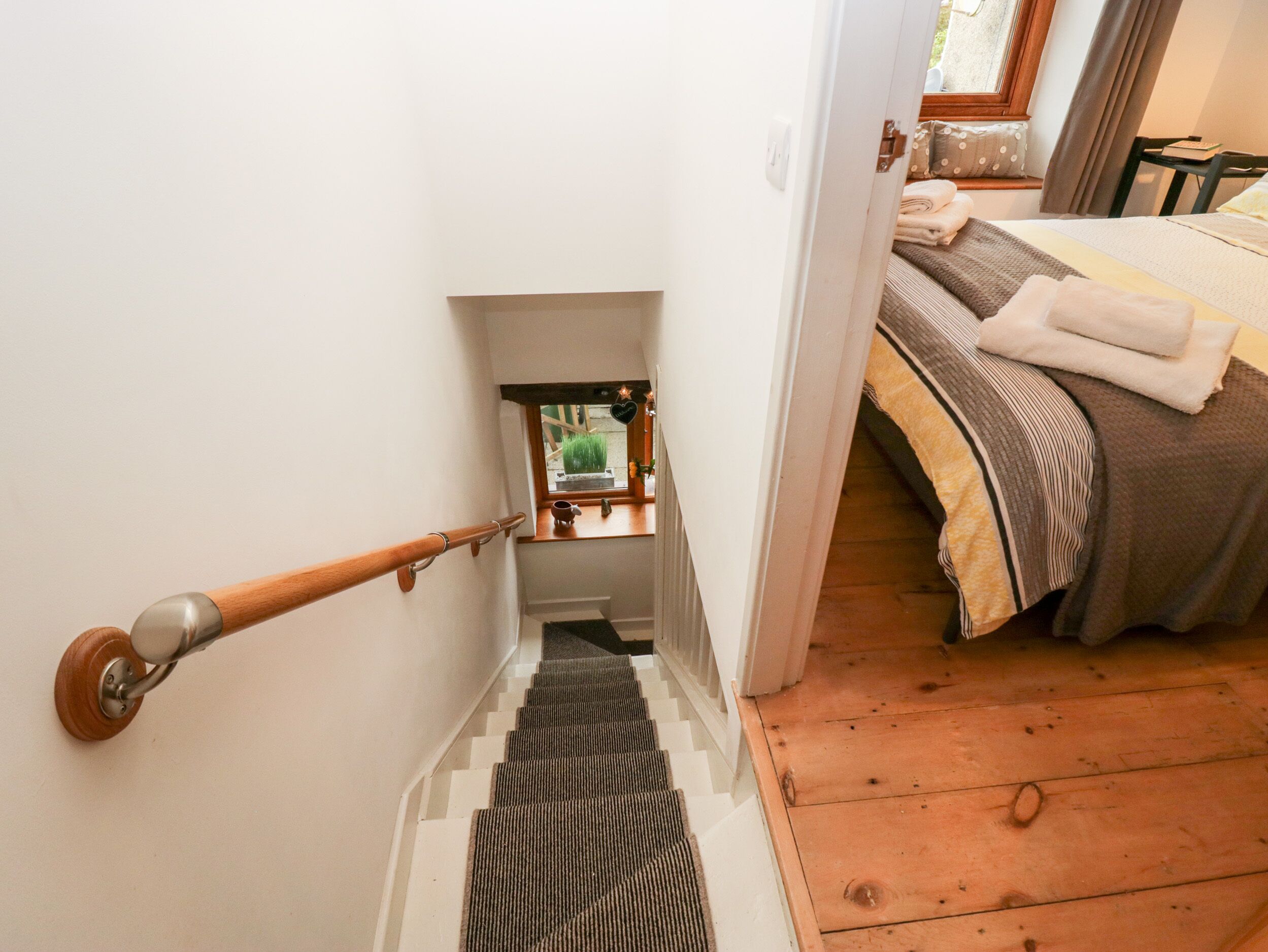 A staircase leading to a bedroom with a bed, a window, and a small table with a cup and a bottle.