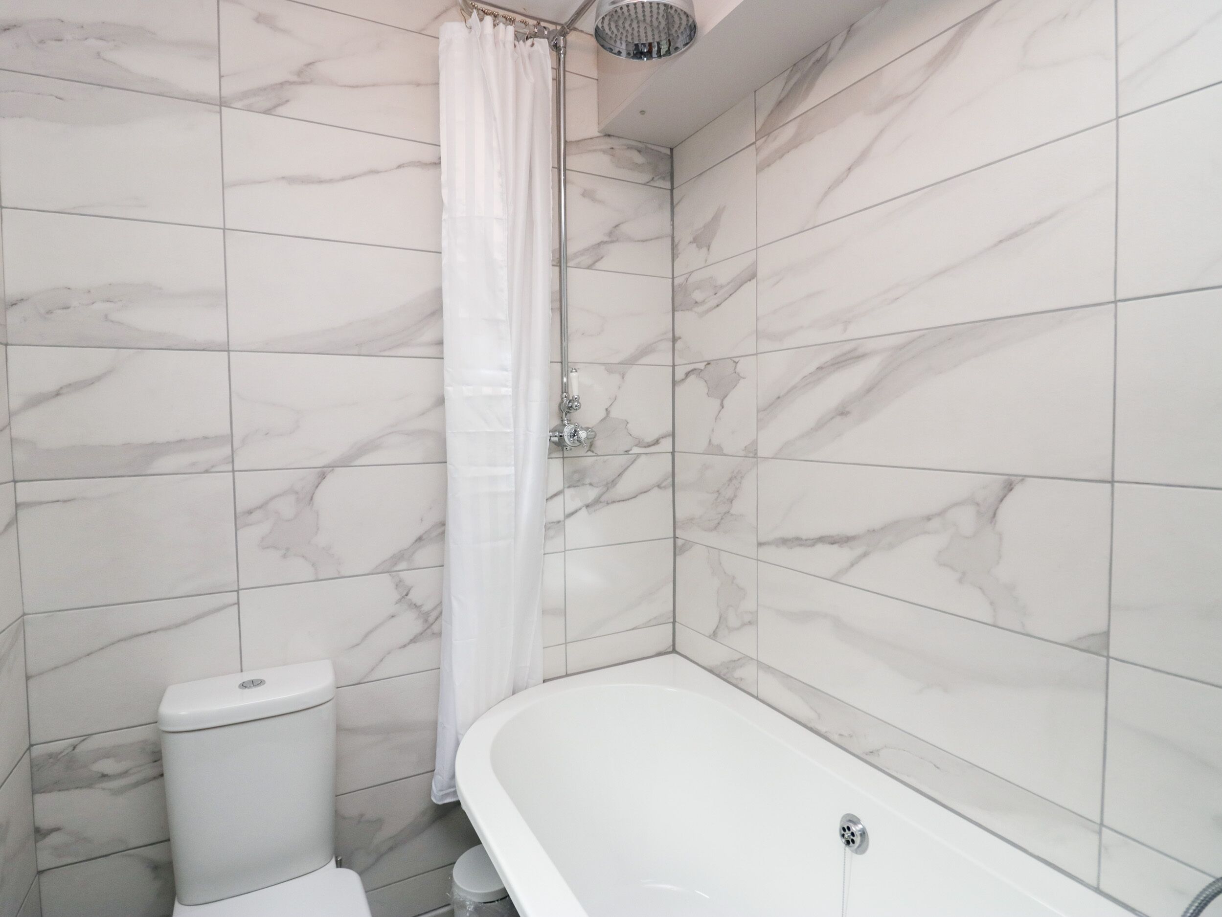 A bathroom with a white bathtub, a toilet, and a shower curtain.