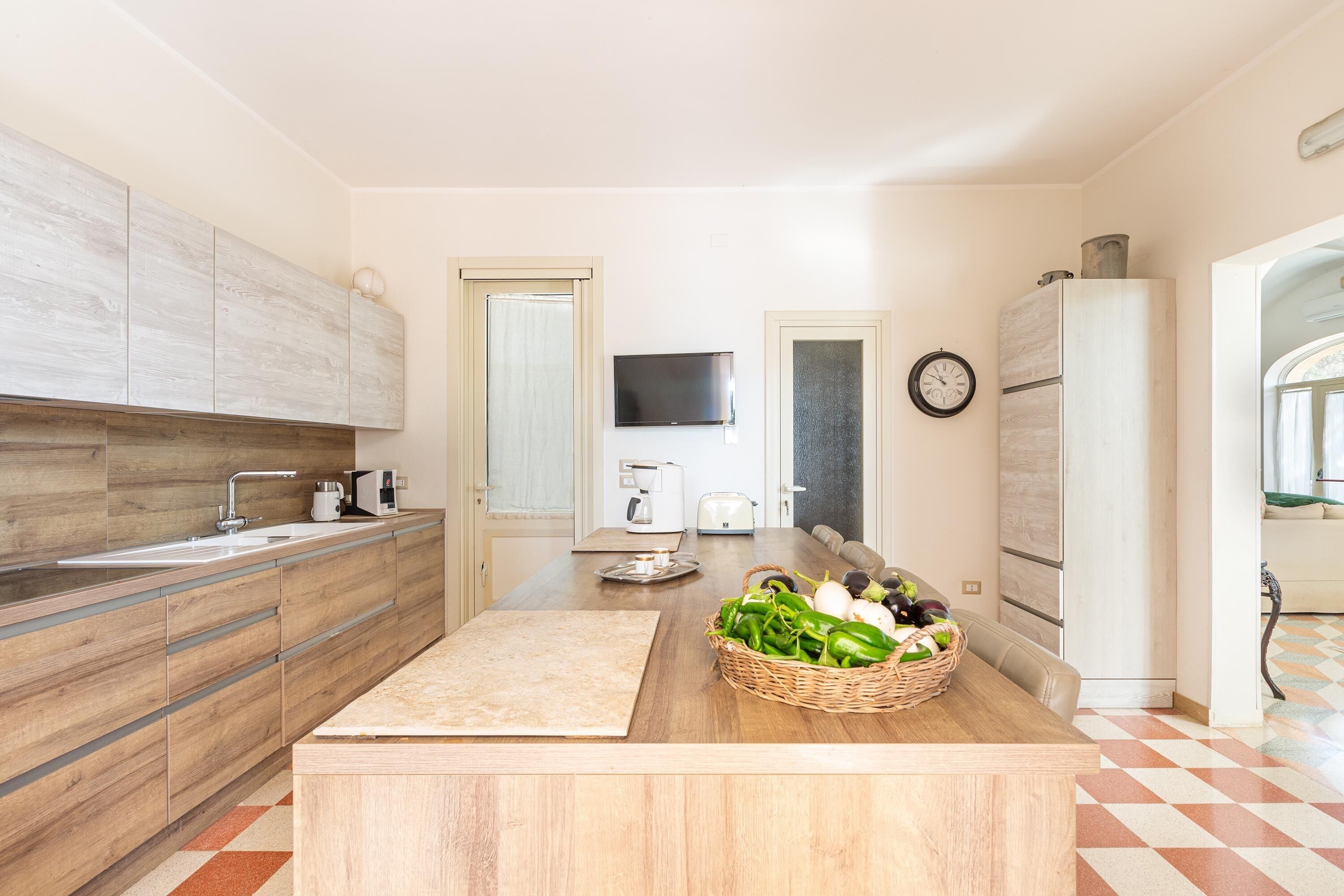 Una cocina moderna con armarios de madera, una isla central, un televisor y un refrigerador.