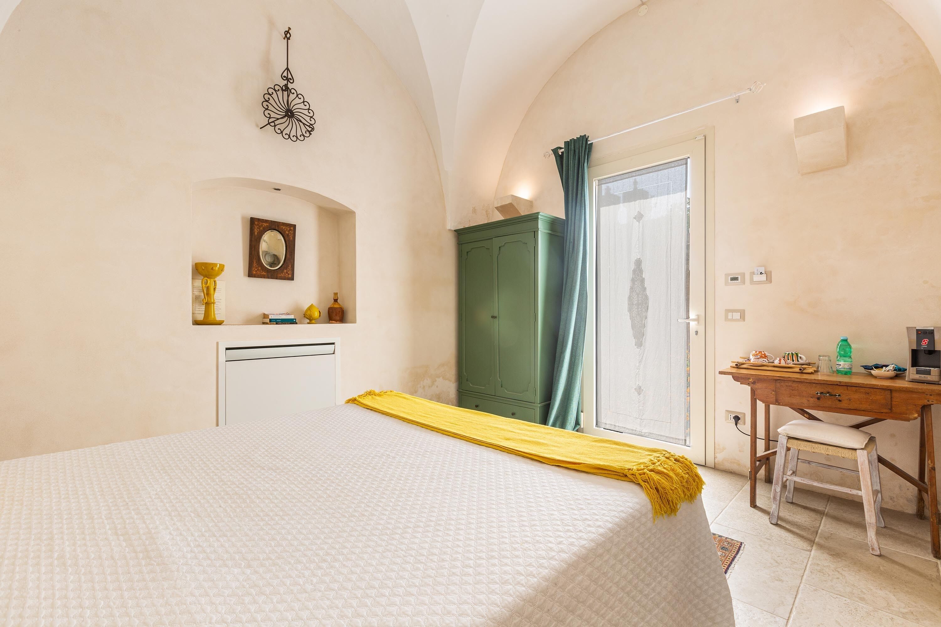 Ein Schlafzimmer mit Bett, Schreibtisch, grünem Kleiderschrank und Spiegel.
