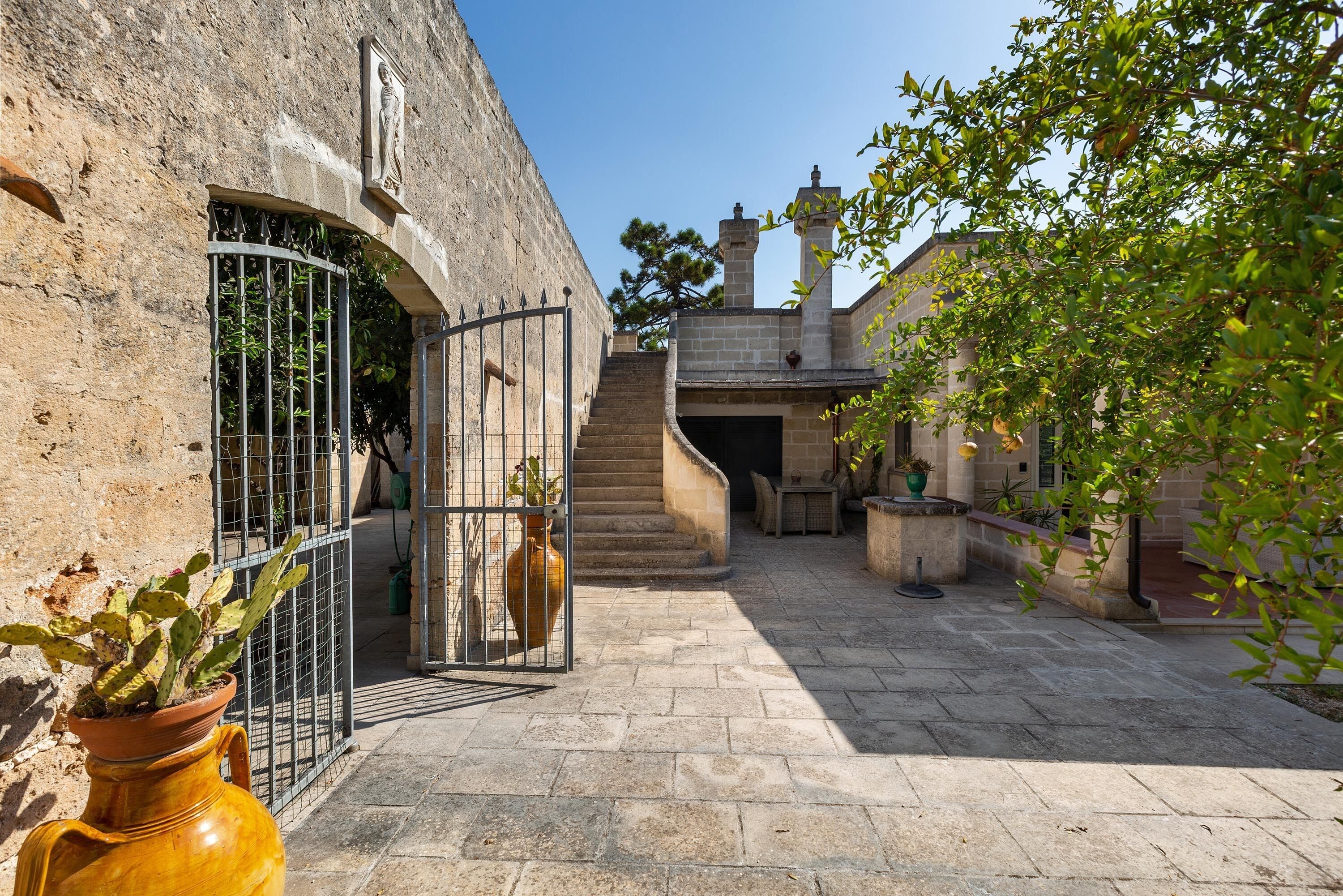 A courtyard with stone walls, a metal gate, and a staircase leading to a building.