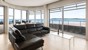 Ein modernes Wohnzimmer mit einer schwarzen Ledersofa, einem Glastisch und großen Fenstern mit Blick auf das Meer.