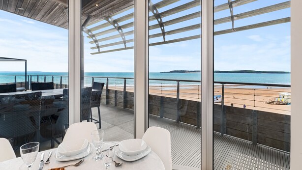 Ein Essbereich mit Tisch für zwei Personen, mit Blick auf einen Strand, eine Holzterrasse und den Meerblick.