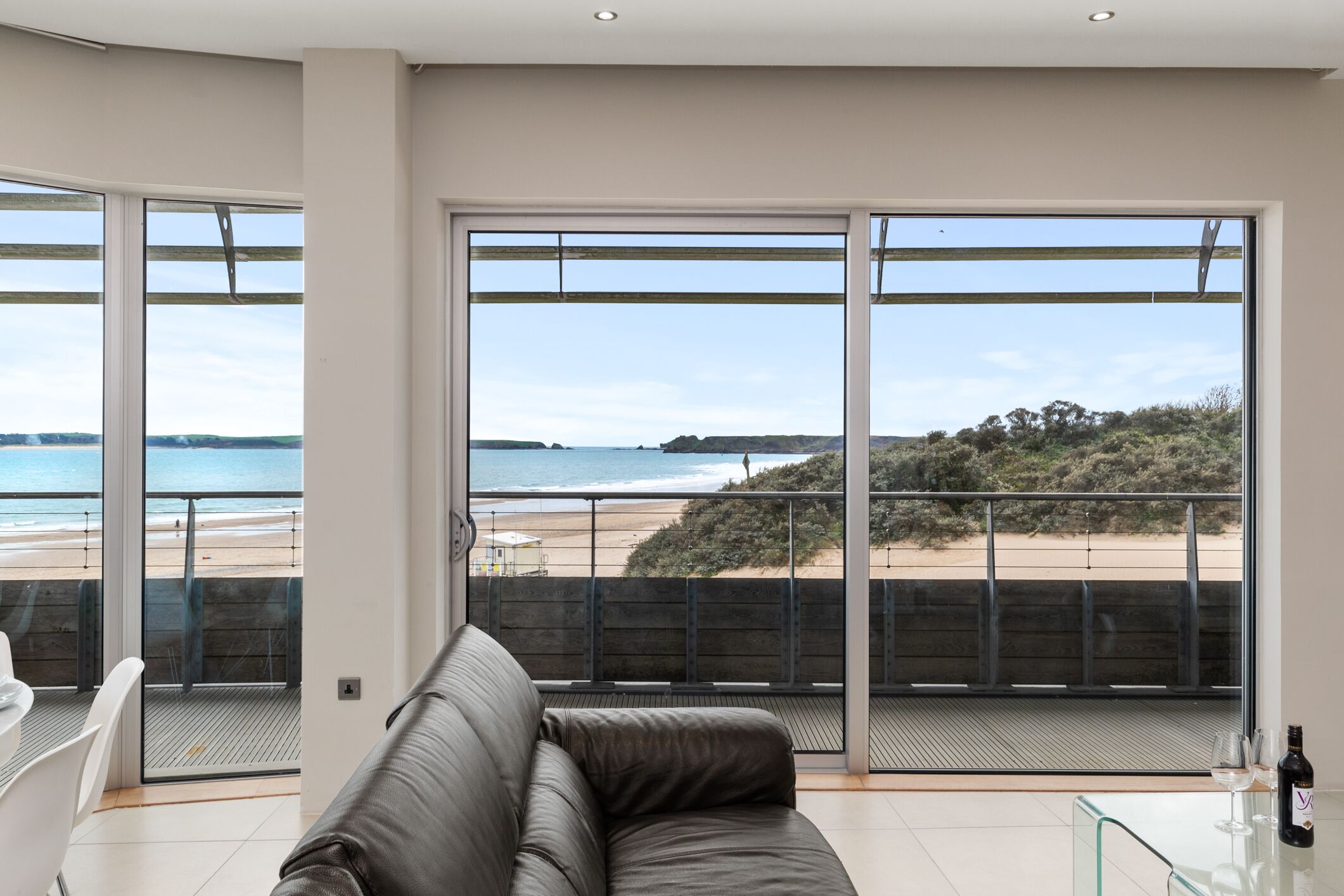 Un salon moderne doté d’une grande porte-fenêtre coulissante donnant sur un balcon avec vue sur la plage.