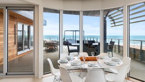 Ein moderner Essbereich mit Meerblick, ausgestattet mit einem großen Esstisch, bequemen Sitzgelegenheiten und einer verglasten Terrasse.