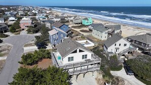 A coastal residential area with houses, some with wooden decks and balconies, and a road leading to the beach.