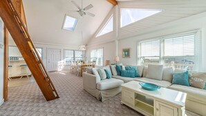 A spacious living room with a high ceiling, a dining area, and a staircase.
