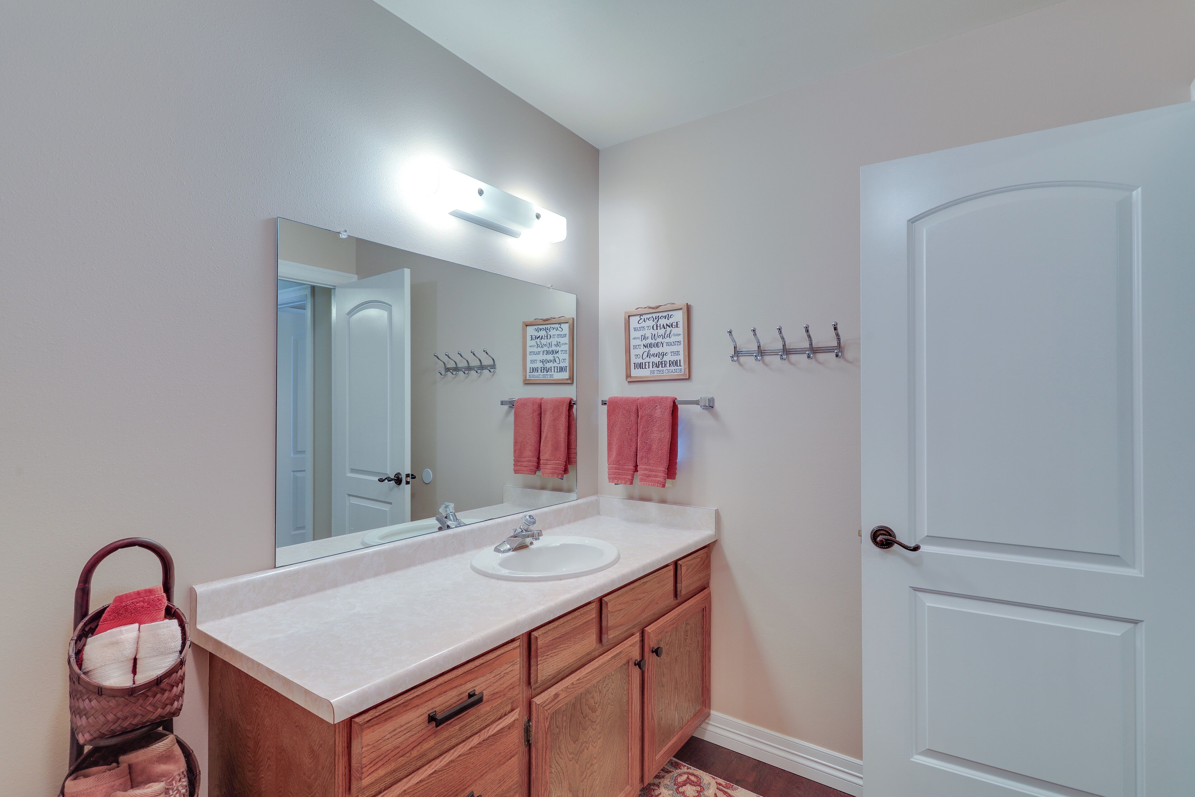 A bathroom with a white sink, wooden vanity, a large mirror, and a white door.