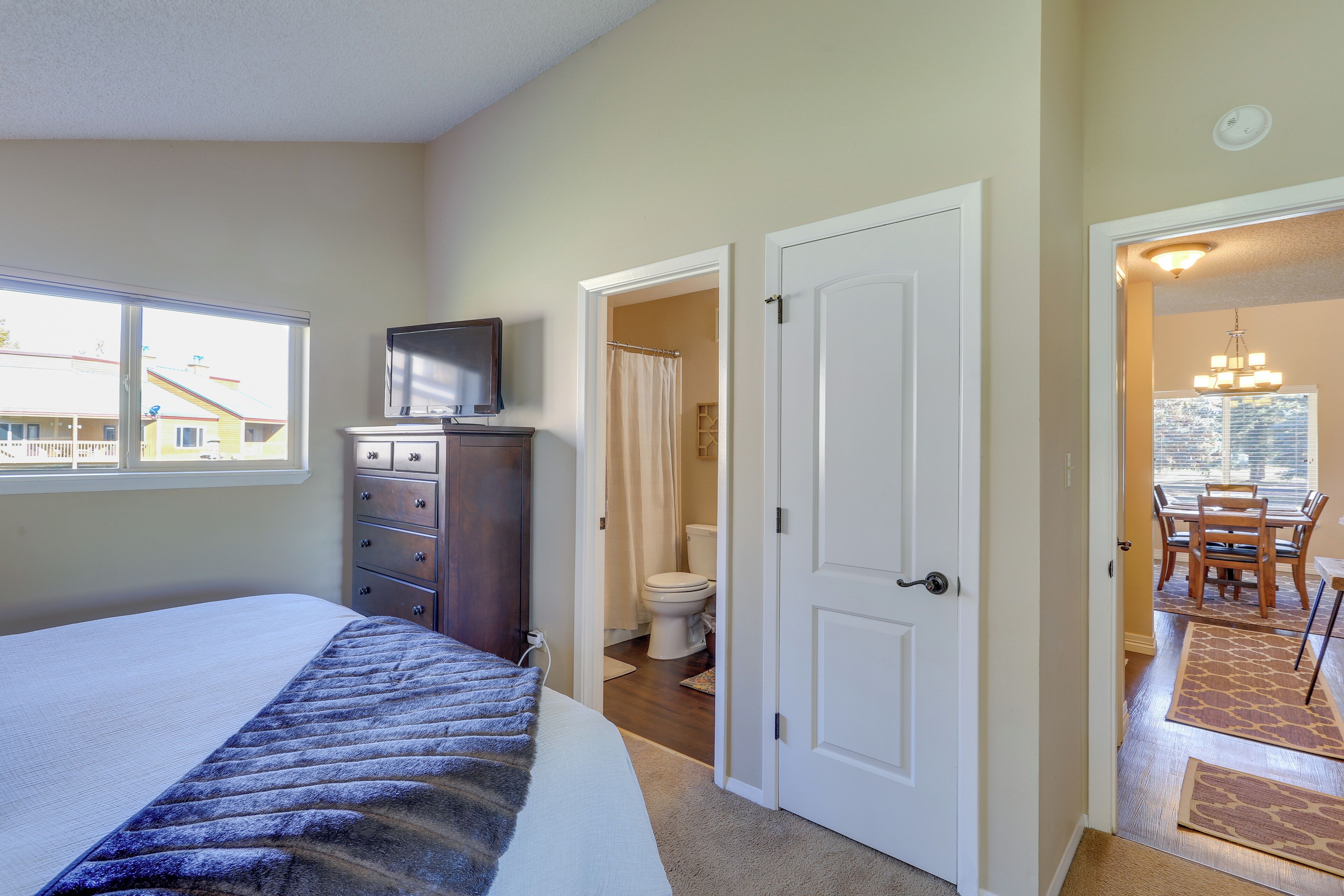 Un dormitorio con cama, cómoda, televisor y baño visible a través de una puerta abierta.
