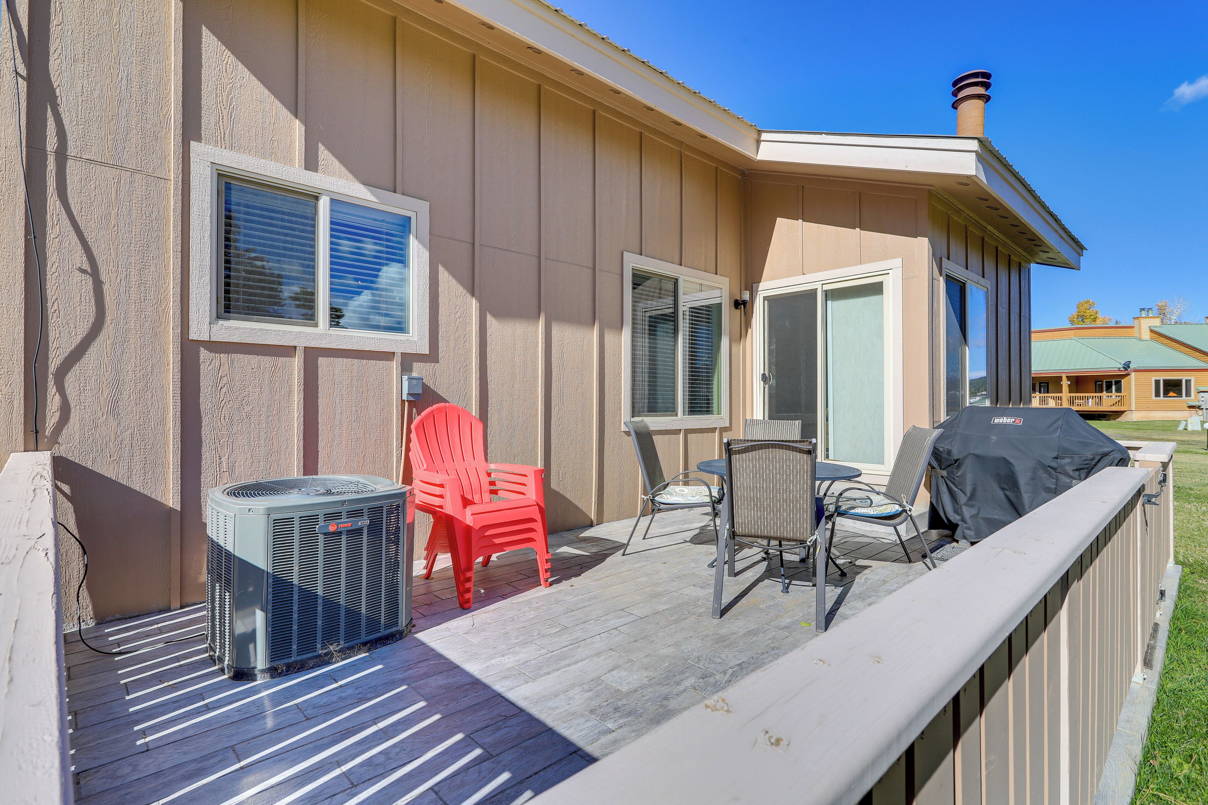 A covered outdoor deck with a grill, chairs, and an air conditioning unit.