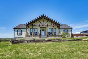 Une maison à deux étages avec un porche à l’avant, des fondations en pierre et une clôture en bois à l’arrière.