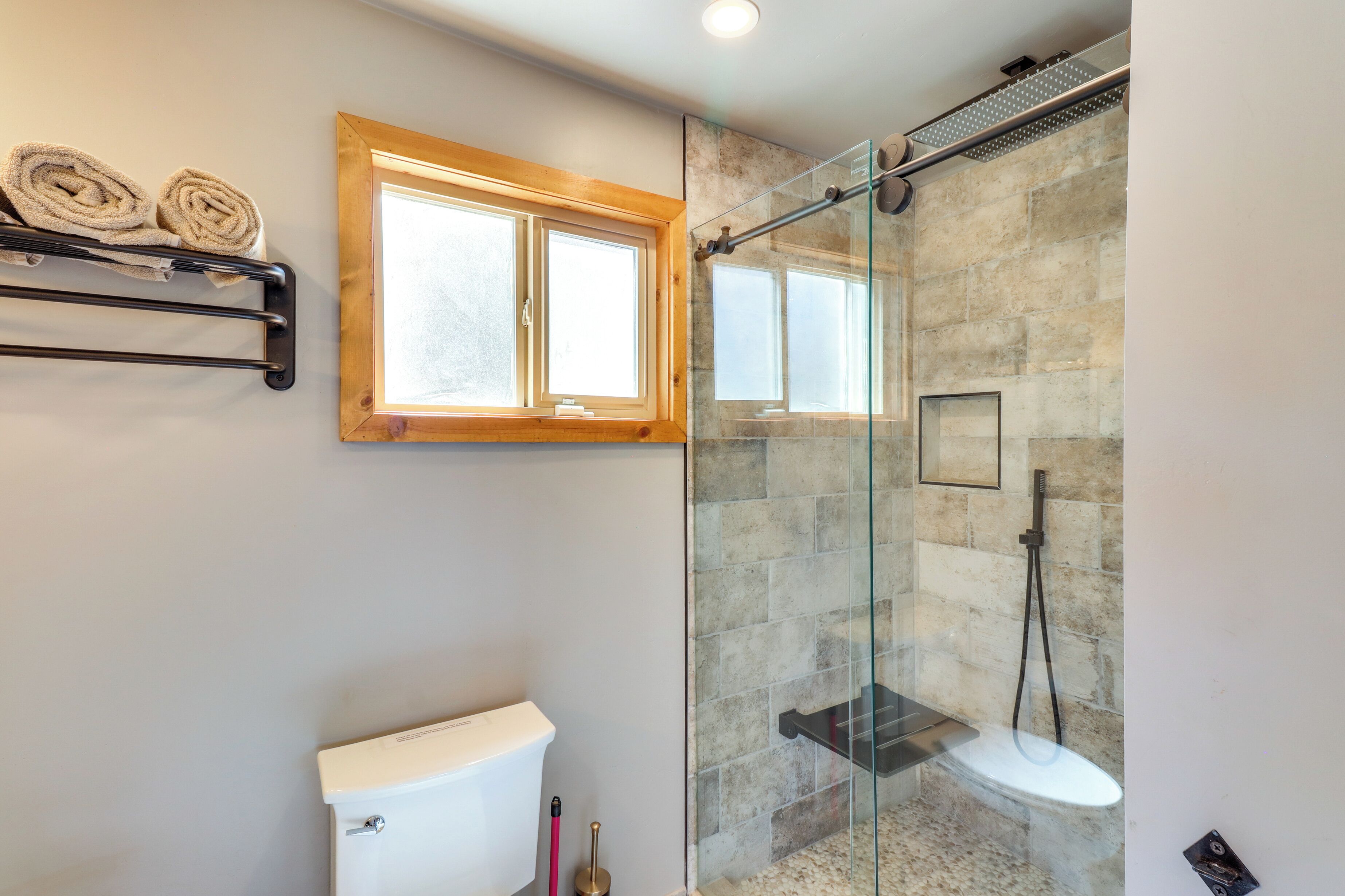 A bathroom with a glass-enclosed shower, a toilet, and a towel rack with towels.