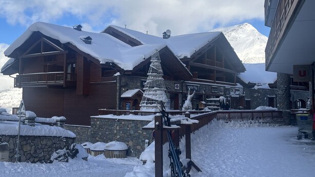 Un edificio cubierto de nieve con un telesilla, muros de piedra y una montaña al fondo.