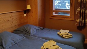 Habitación con dos camas, cabecera de madera, ventana con vistas a la montaña y una lámpara en la pared.