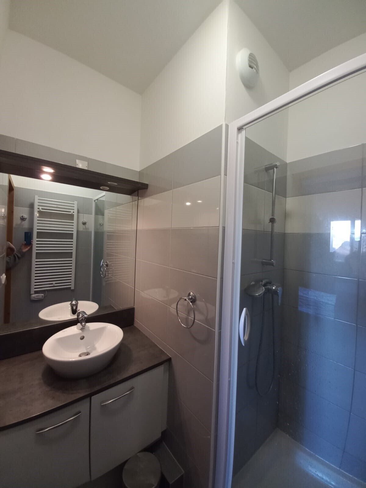 A modern bathroom with a glass-enclosed shower, a large mirror, and a vanity with a sink and cabinet.
