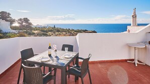 A terrace with a table set for two, overlooking the sea, with a white building and a lighthouse in the background. - Apartment Buenos Momentos (Carvoeiro)