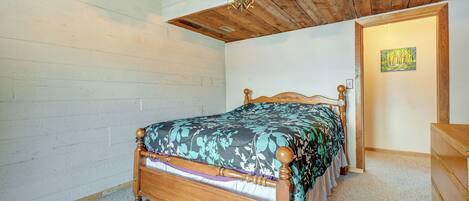A bedroom with a wooden bed, a wooden dresser, a white wall, and a wooden ceiling.