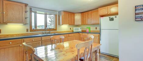 Una cocina con armarios de madera, una mesa de comedor, sillas, un refrigerador y una ventana.