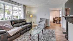 A living room with a leather sofa, a glass coffee table, a grey armchair, and a dining area in the background. - Central Auburn Apartment w/ Porch: Pets Welcome! (Auburn)