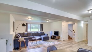 A modern living room with a grey sectional sofa, a round coffee table, and a TV stand. - Serene Palmer Home: Walk to Downtown & Riverfront! (Palmer)