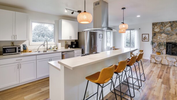 A modern kitchen with white cabinetry, a stainless steel refrigerator, a large island with bar stools, and pendant lighting. - Serene Palmer Home: Walk to Downtown & Riverfront! (Palmer)