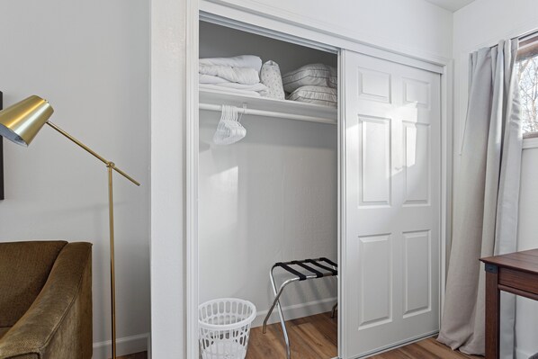 A room with a closed wardrobe, a brown chair, a gold floor lamp, and a window with curtains.