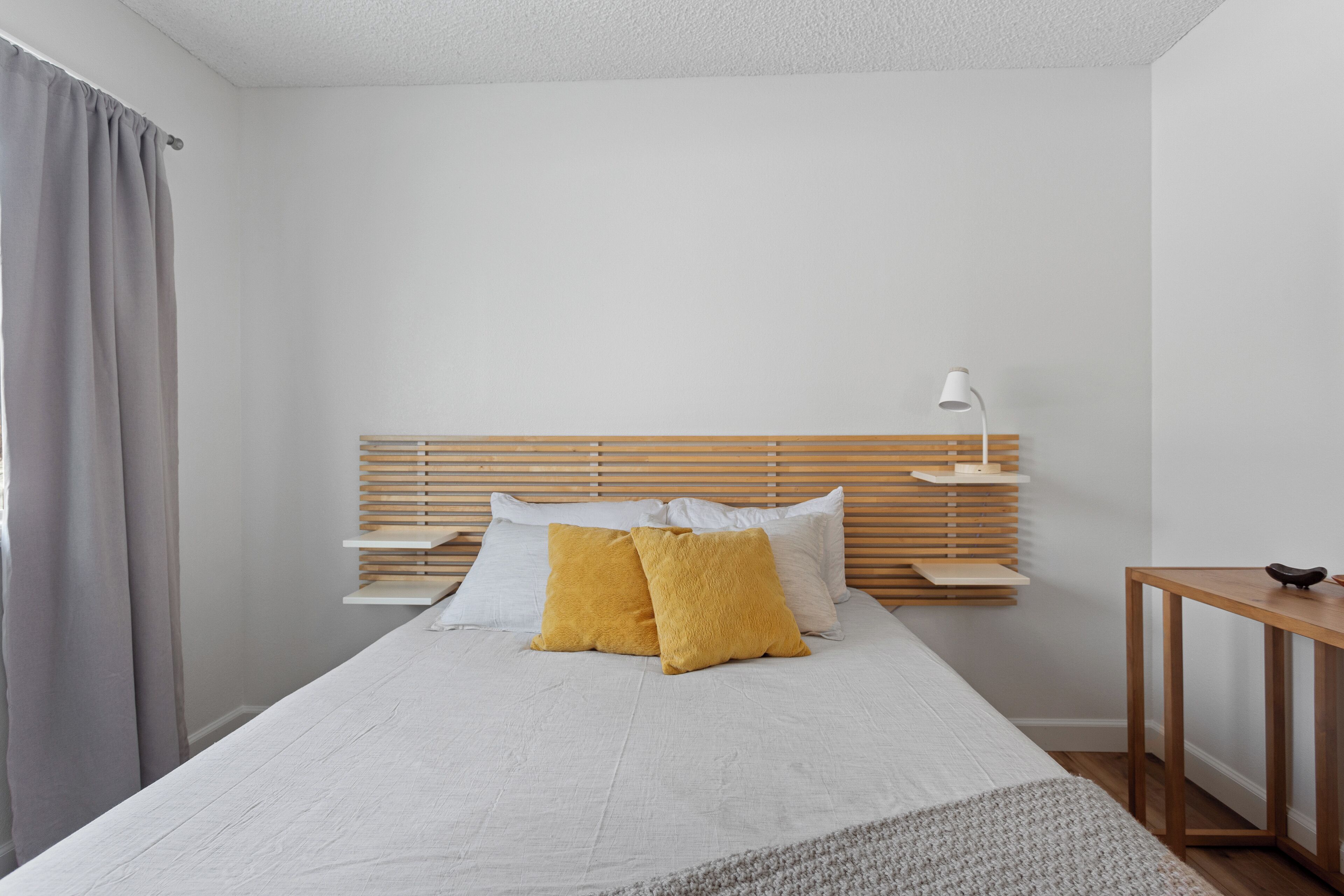 Une chambre à coucher avec un lit, une table de chevet, une lampe et une fenêtre avec des rideaux.