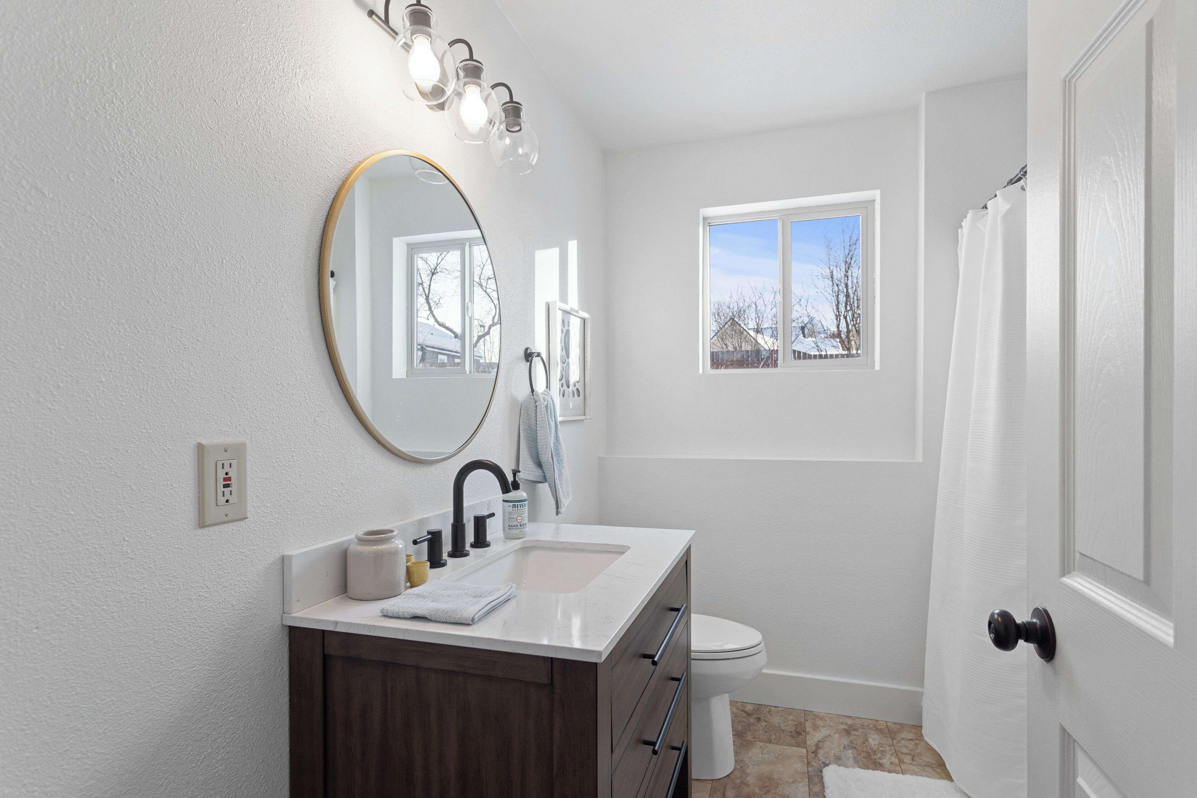 A bathroom with a white vanity, a round mirror, a sink, and a toilet.