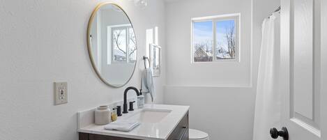 A bathroom with a white vanity, a round mirror, a sink, and a toilet.