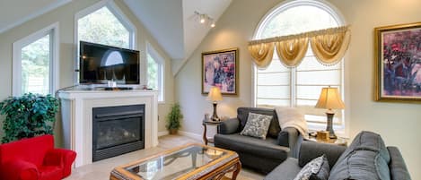 A spacious living room with a fireplace, a television, and a large window with curtains.