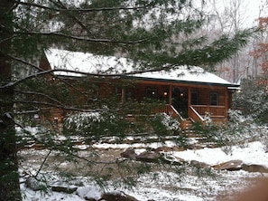 Eine Hütte mit Veranda, umgeben von verschneitem Gelände und Bäumen.