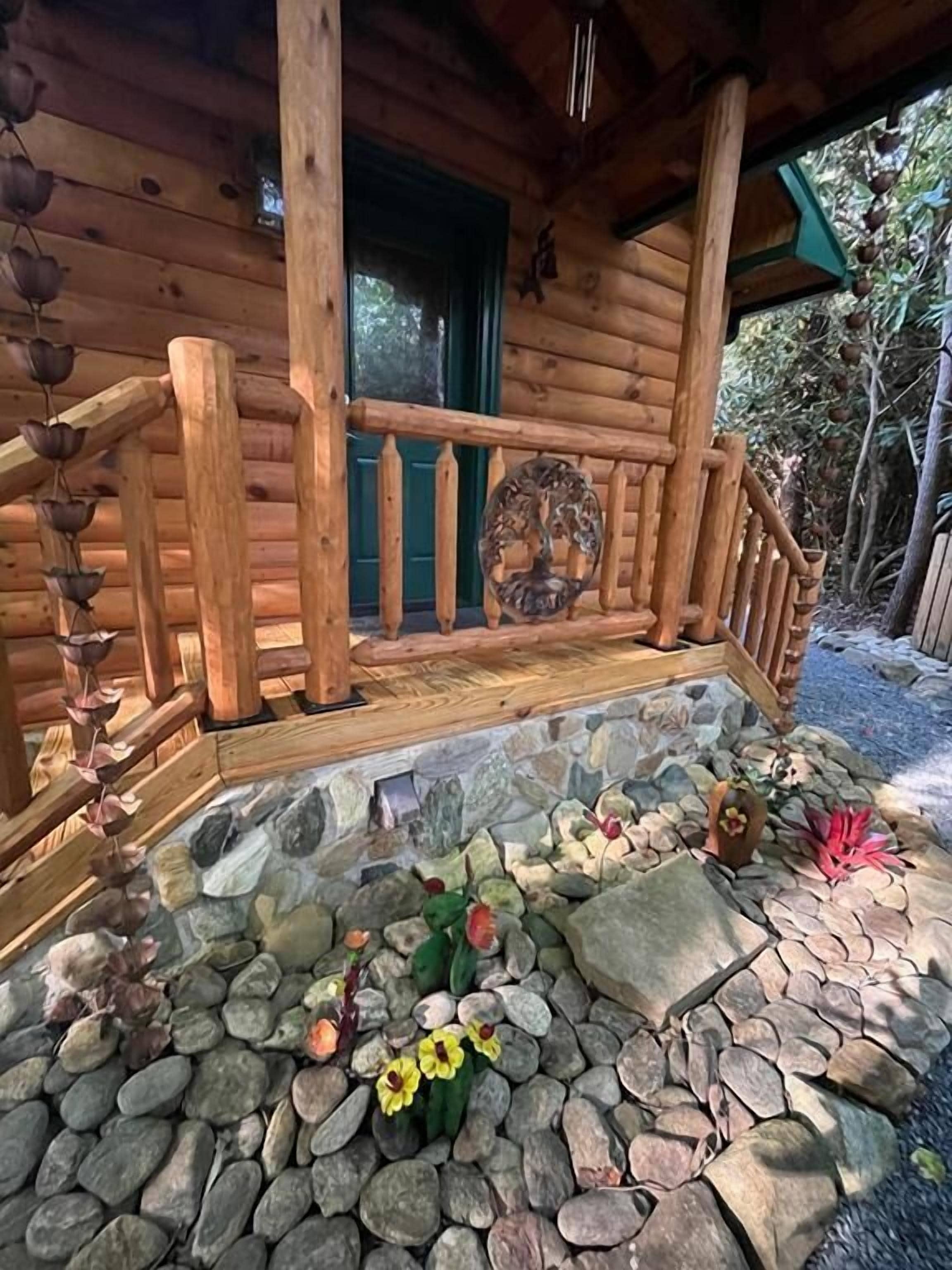 A wooden cabin with a stone-paved porch, a wooden railing, and a door with a green frame.