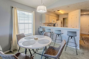 A dining area with a round table, four chairs, and a kitchen in the background.