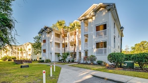 A multi-story residential building with balconies, a well-maintained lawn, and a clear sky. - Myrtle Beach Oasis Condo w/ Pool Access! (Myrtle Beach)