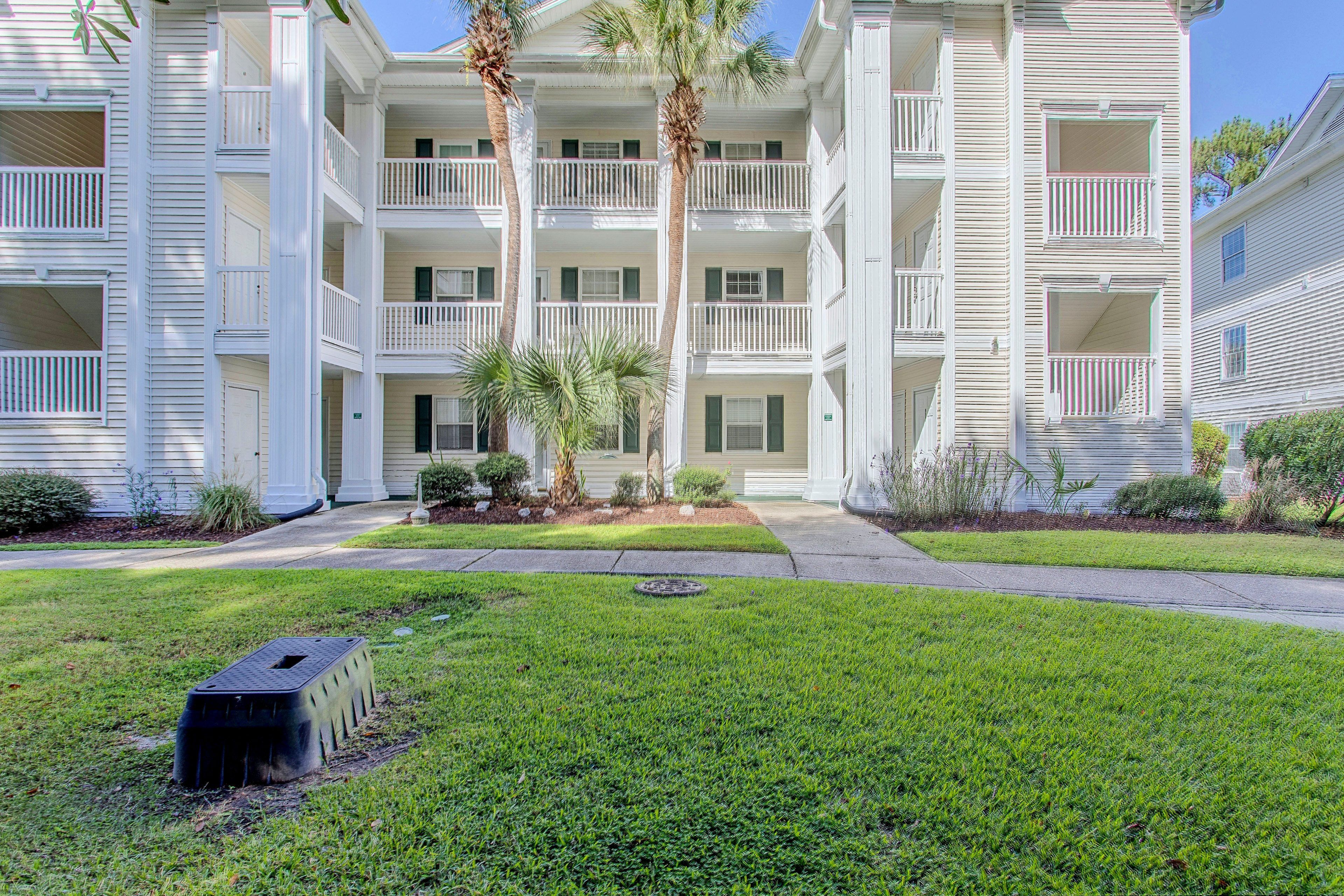 A multi-story building with balconies, a well-maintained lawn, and a pathway leading to the entrance.