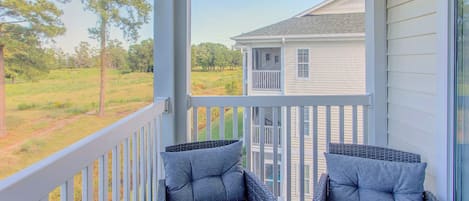 A porch with two wicker chairs and a view of a house and trees.